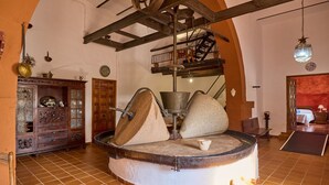 A traditional mill with a stone base and a wooden structure above, surrounded by rustic decor and a tiled floor. - MOLINO DE LOS CARDENES 1911 (Montoro)