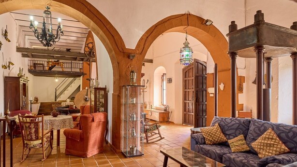 A spacious living area with a high ceiling, exposed brick arches, a large sofa, a coffee table, and a fireplace. - MOLINO DE LOS CARDENES 1911 (Montoro)