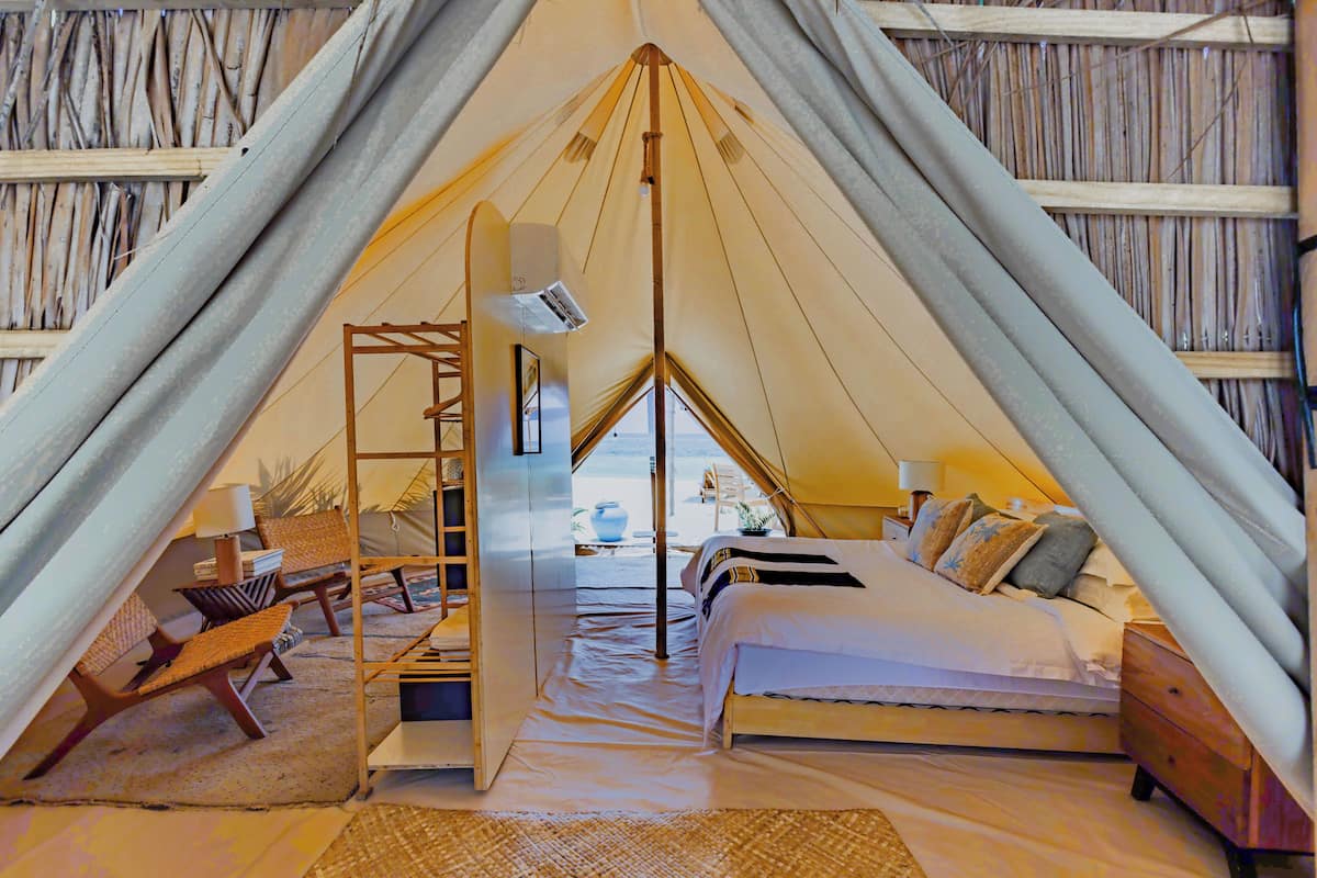 Una habitación acogedora con forma de triángulo, estilo tienda de campaña, con cama, una escalera y una pequeña mesa con sillas.