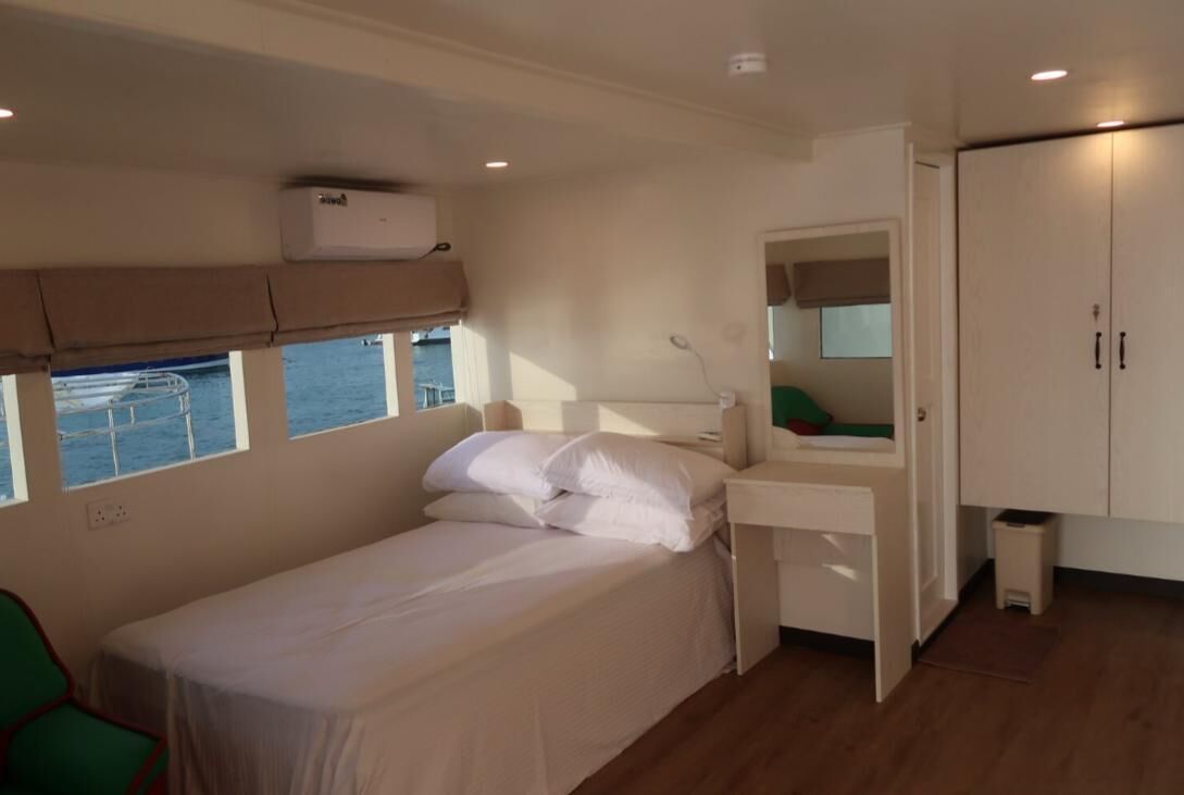 Une chambre individuelle avec un lit simple, une fenêtre, un bureau avec un miroir et une armoire.