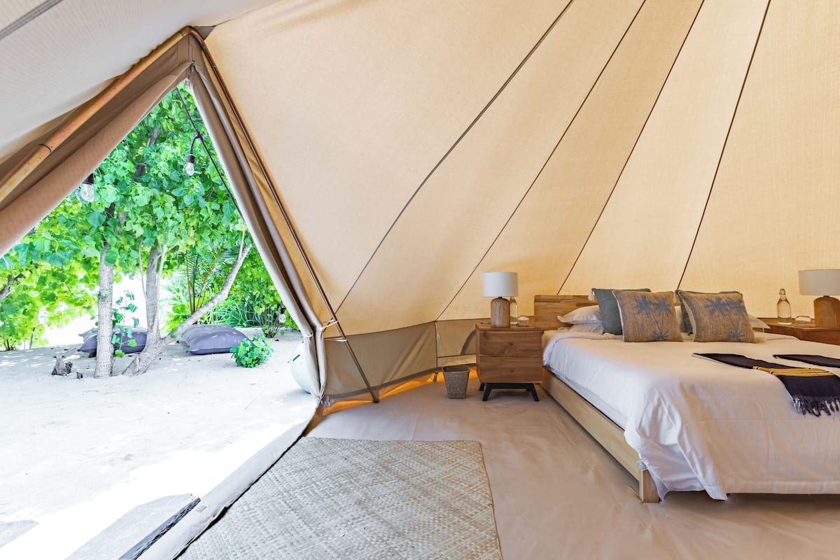 Alojamiento con tienda de campaña, cama, mesitas de noche y vistas al follaje exterior.