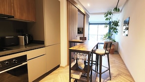 A modern kitchen with wooden cabinets, a black countertop, and a built-in oven. There is a dining area with a wooden table and chairs, and a large window providing natural light. - Peaceful, central apartment in a quiet, tree-lined street, rare in Casablanca. (Casablanca)