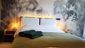A neatly made bed with a green bedspread and two folded towels, a nightstand with a lamp, and a wall mural of palm trees. - Peaceful, central apartment in a quiet, tree-lined street, rare in Casablanca. (Casablanca)