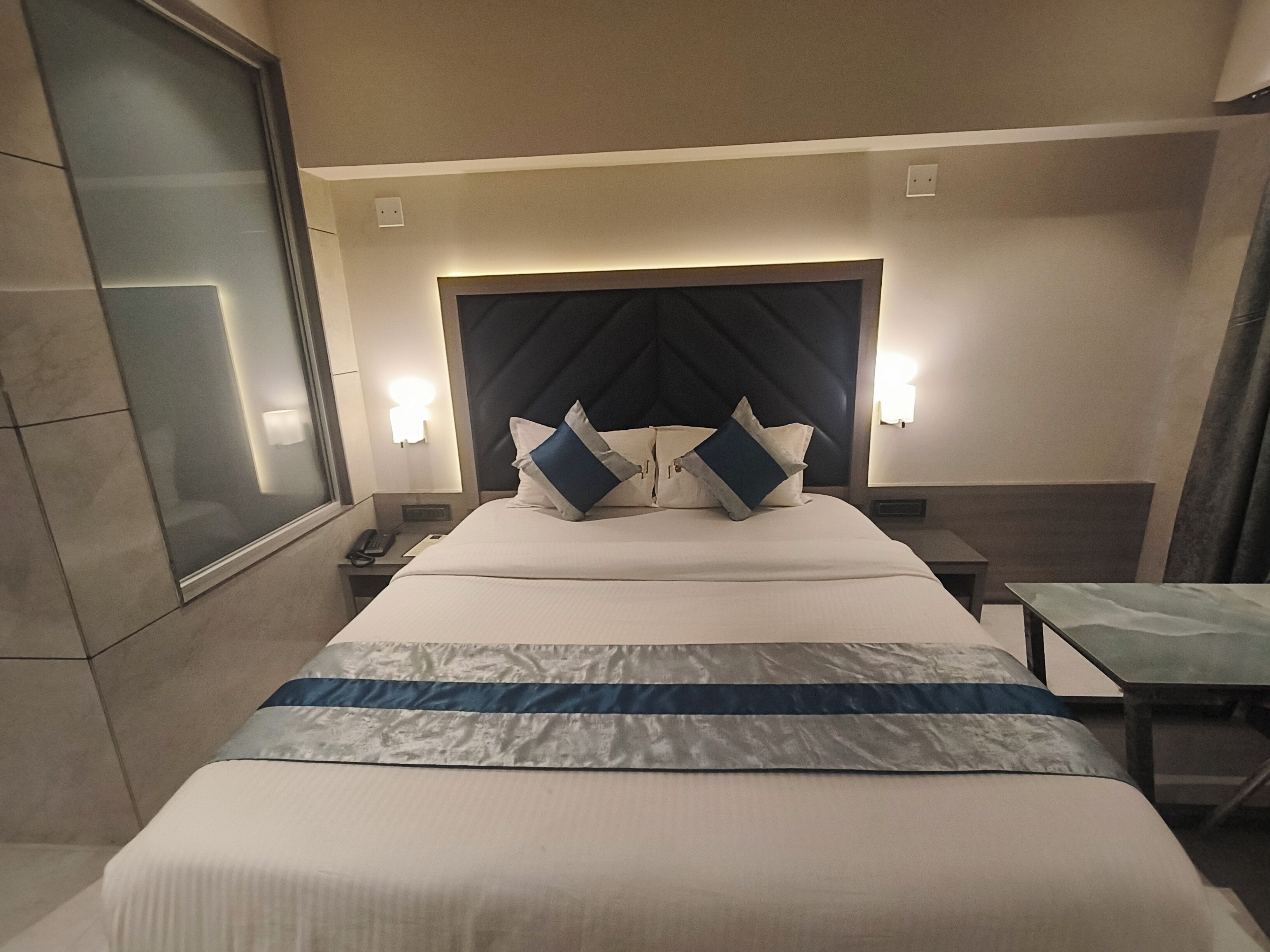 A hotel room with a large bed, two bedside tables, a nightstand, a window, and a chair.