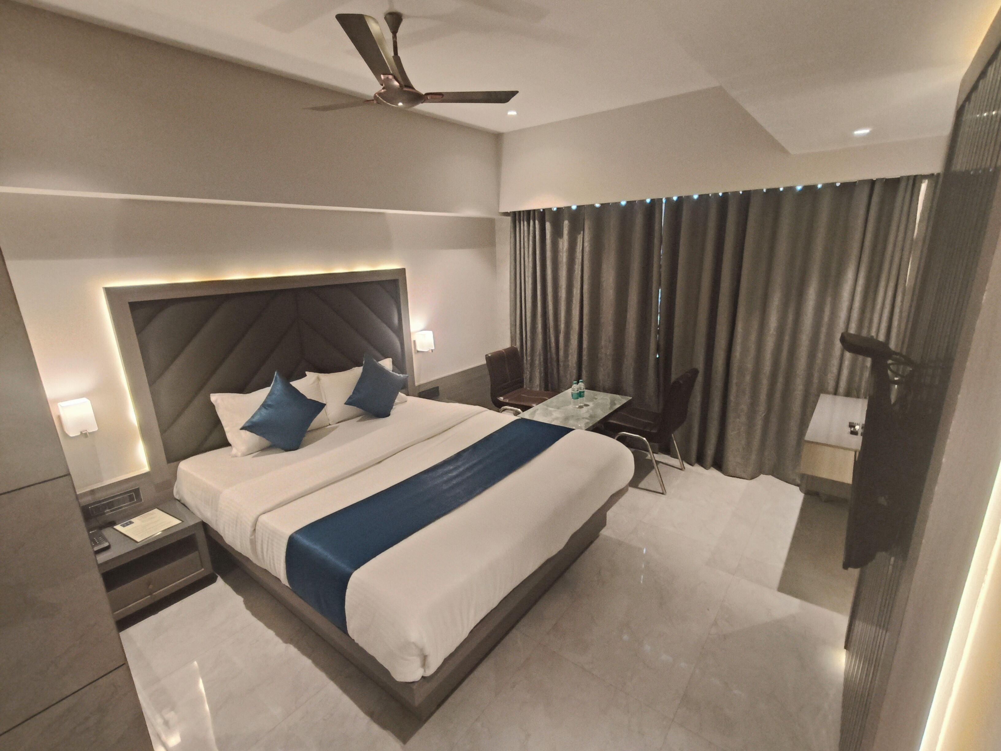 A modern hotel room with a large bed, a ceiling fan, a desk with a chair, and a bathroom with a shower and toilet.