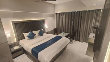 A modern hotel room with a large bed, a ceiling fan, a desk with a chair, and a bathroom with a shower and toilet.