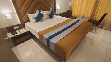 A hotel room with a large bed, a bedside table with a phone and a notepad, a chair, a small table with a bottle, and a curtain.