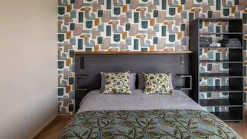 Ein modernes Schlafzimmer mit einer Wand im geometrischen Muster, einem dunklen Kopfteil, einer grauen Bettdecke und einer gemusterten Tagesdecke.
