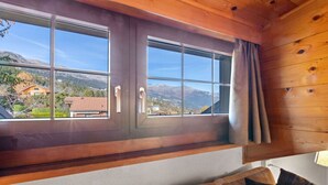 A room with a large window offering a mountain view, a wooden ceiling, and a sofa with cushions. - Montana Village - appartement rénové, 5 pers (Montana Village)