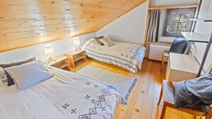A cozy attic bedroom with a sloped ceiling, a bed with patterned bedding, a bedside table with a lamp, a small desk, and a window with curtains. - Montana Village - appartement rénové, 5 pers (Montana Village)