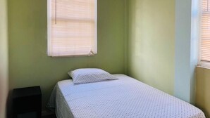 A small, single-bed room with a window and a nightstand.