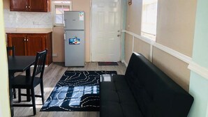A compact kitchen with wooden cabinets, a refrigerator, and a dining area with a black sofa and chairs.