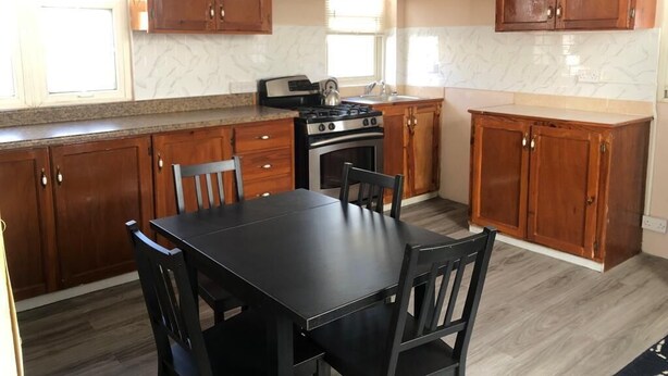 A kitchen with wooden cabinets, a black countertop, a stove, and a dining table with chairs.