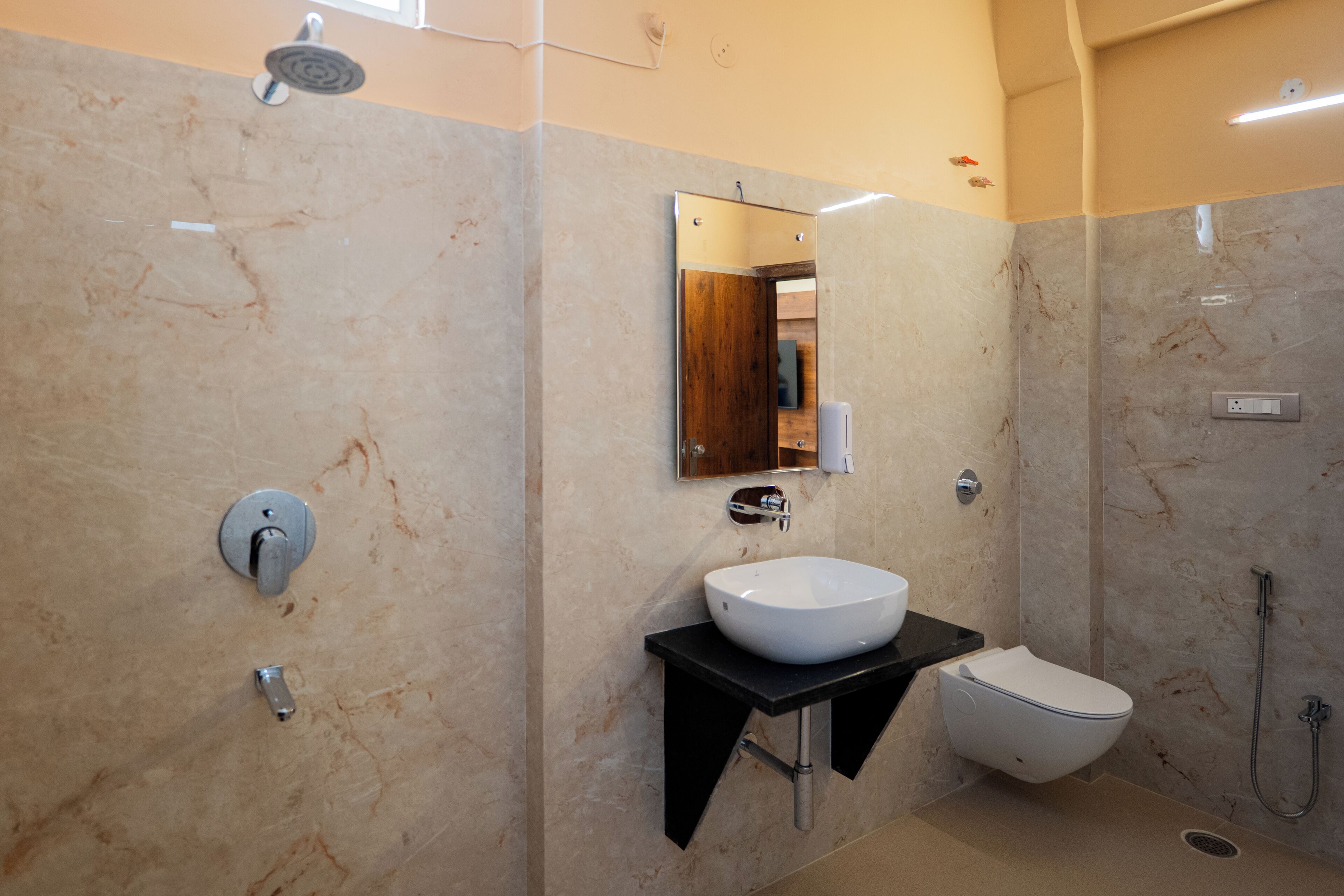 A modern bathroom with a marble wall, a white sink, a black countertop, a toilet, and a shower.