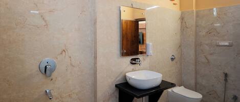 A modern bathroom with a marble wall, a white sink, a black countertop, a toilet, and a shower.
