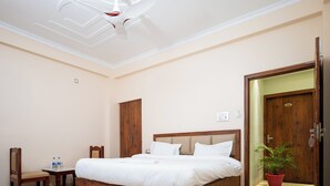A bedroom with a wooden bed, a wooden wardrobe, a small table with chairs, a potted plant, and a ceiling fan.