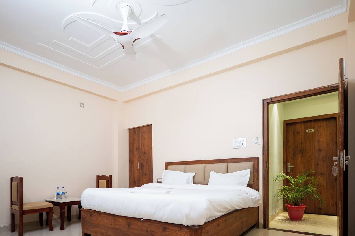 A bedroom with a wooden bed, a wooden wardrobe, a small table with chairs, a potted plant, and a ceiling fan.