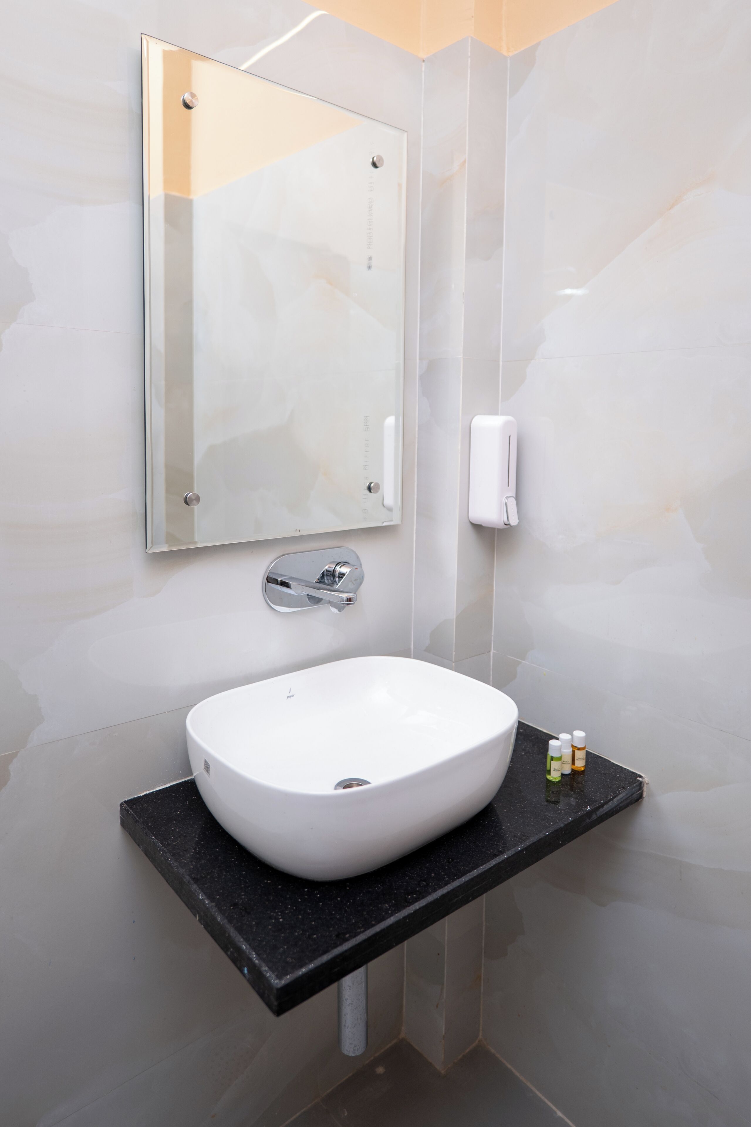 Un baño con un lavabo blanco, un espejo y un dispensador de jabón.