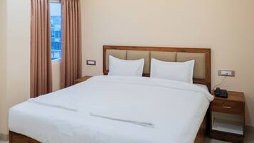 A neatly made bed with white linens, a wooden headboard, and a bedside table with a phone.
