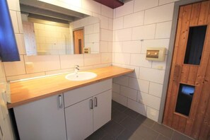 Une salle de bain avec un meuble-lavabo en bois, des carreaux blancs, un miroir et une porte en bois.