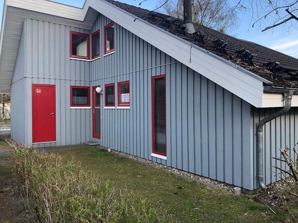 Un bâtiment gris avec une porte rouge, de nombreuses fenêtres et un toit en pente.