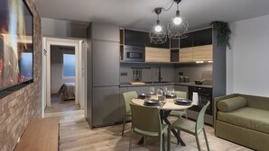A modern kitchen with a dining area, featuring a wooden table, green chairs, and a green sofa.