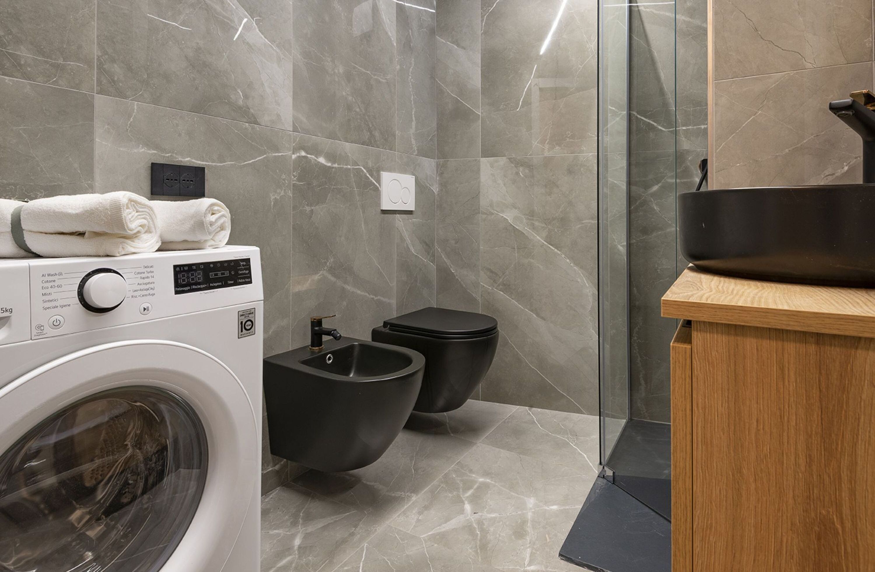 A modern bathroom with a washing machine, bidet, and a wooden vanity.