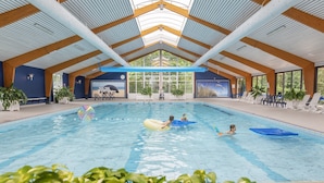 Piscina interna com teto alto, vigas de madeira e grandes janelas.