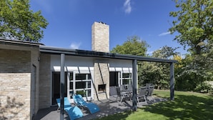 Uma casa moderna com fachada de tijolos, uma chaminé e um alpendre coberto com móveis de exterior.