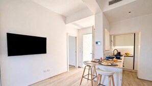 Una cocina moderna con un televisor de pantalla plana montado en la pared, una pequeña isla con taburetes y una puerta visible que da a otra habitación.