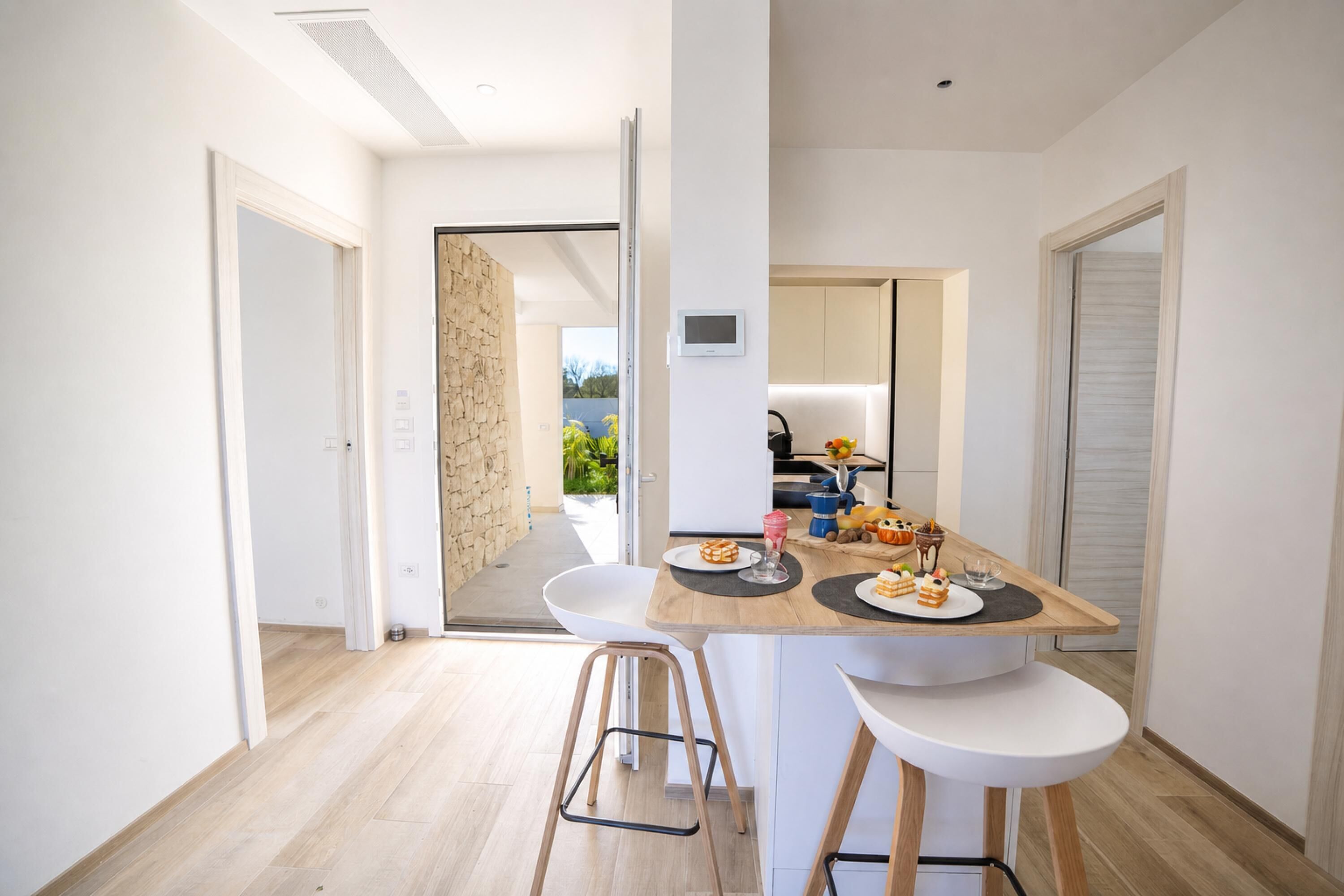 A modern kitchen with a dining table, two white chairs, and a view of the outside.