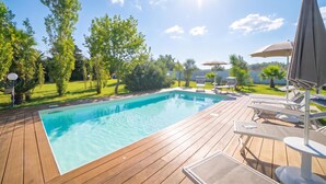 Una terraza de madera con piscina, sillas de descanso y sombrillas.