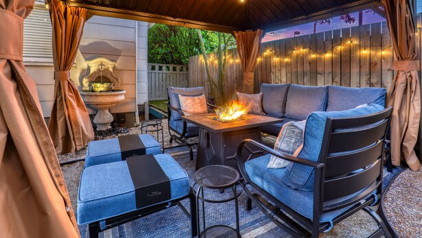 An outdoor patio with a fire table, blue cushioned seating, and string lights. - Walker’s Delight on Queen Anne (Seattle)