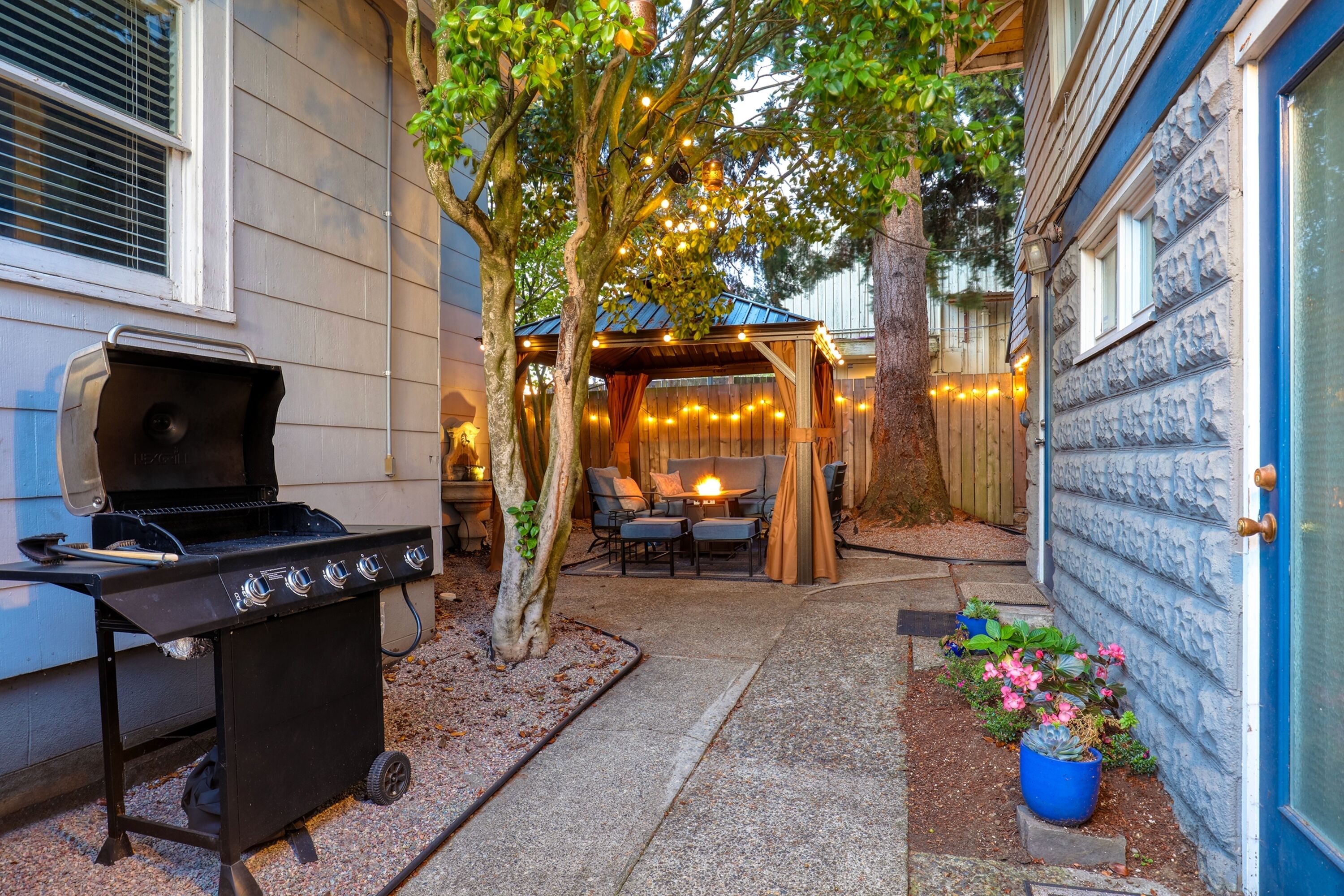 A backyard with a grill, outdoor seating, string lights, and potted plants.