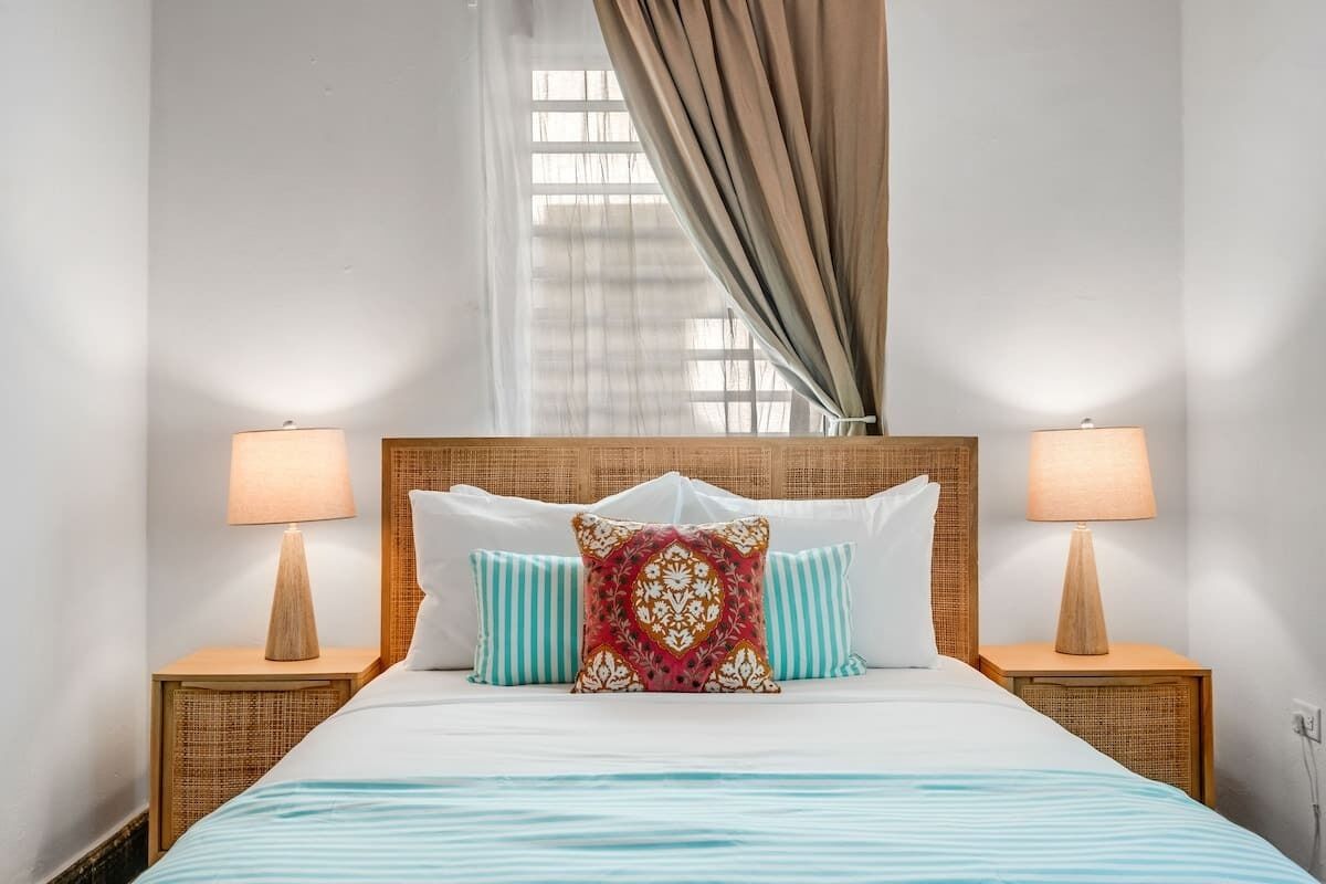 Een opgemaakt bed met gestreept beddengoed, twee bedlampjes en een decoratief kussen.
