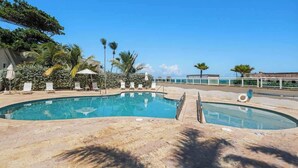 Una piscina amb gandules i ombrel·les, envoltada de palmeres i un cel serè.