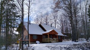 A wooden lodge with a porch and a snow-covered roof, surrounded by trees.