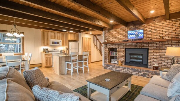 A spacious living room with a fireplace, a kitchen with wooden cabinets, and a dining area with a table and chairs.