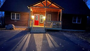 A wooden cabin with a red door, a porch with railings, and a driveway leading to the entrance.