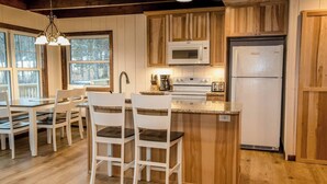 A kitchen with wooden cabinets, a microwave, a refrigerator, and a dining area with white chairs.