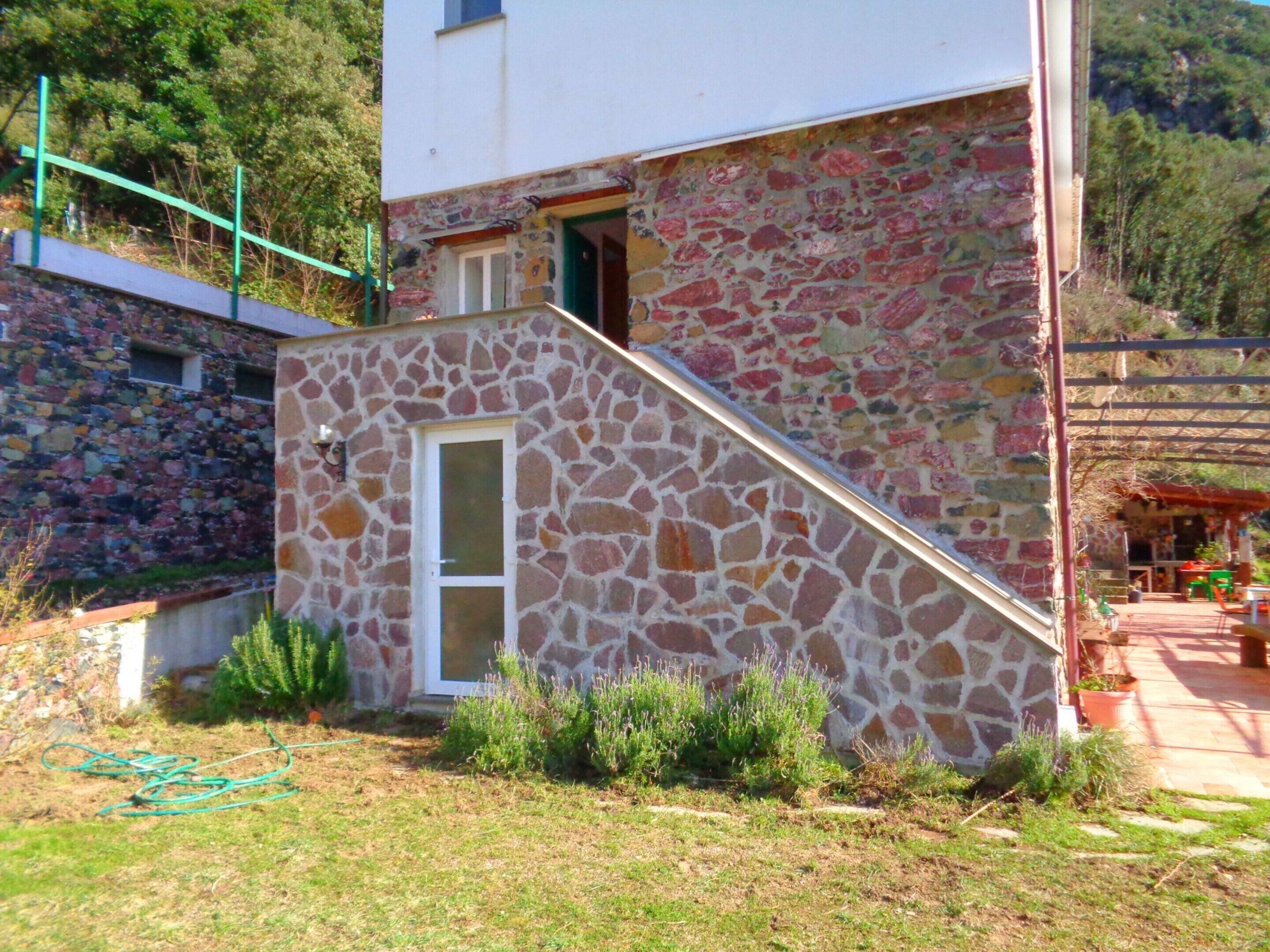 A stone building with a small staircase leading to a door, surrounded by grass and plants.