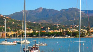 Una marina con veleros, un pueblo costero y montañas al fondo.