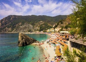 A coastal beach with clear turquoise waters, rocky cliffs, and a row of beachside buildings with umbrellas. - Hillside Retreat Near 5 Terre (Casarza Ligure)