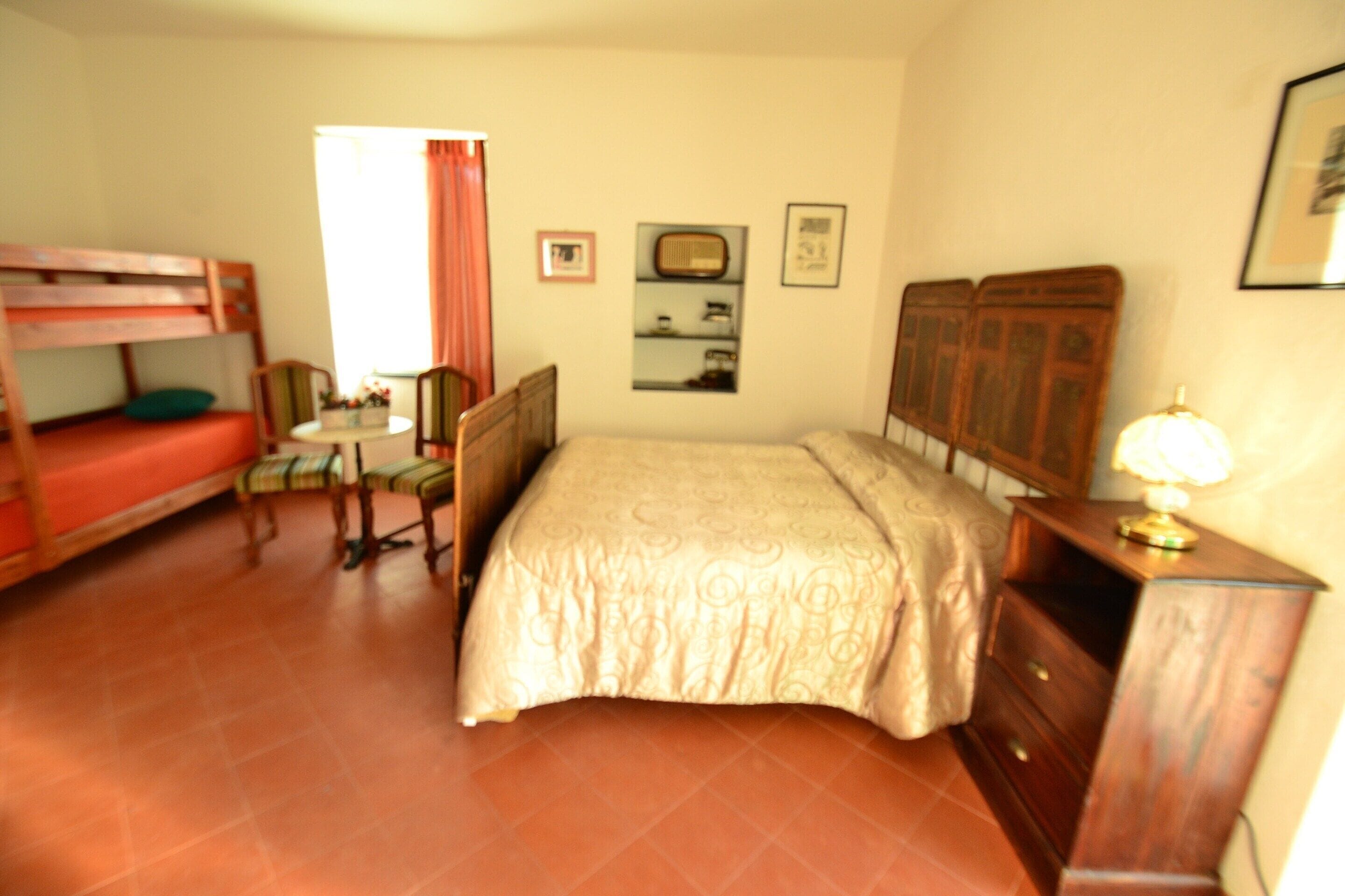 Une chambre avec un lit superposé, une petite table, une chaise, une commode et une lampe.