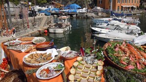 Un montaje para comer frente al agua, con platos de mariscos y barcos al fondo.