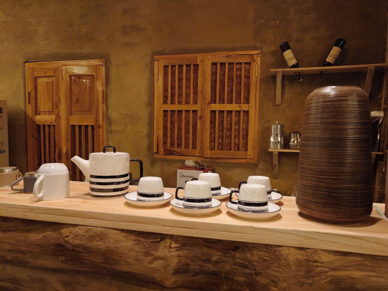 A coffee station with a coffee maker, teapot, cups, and a large cylindrical container.