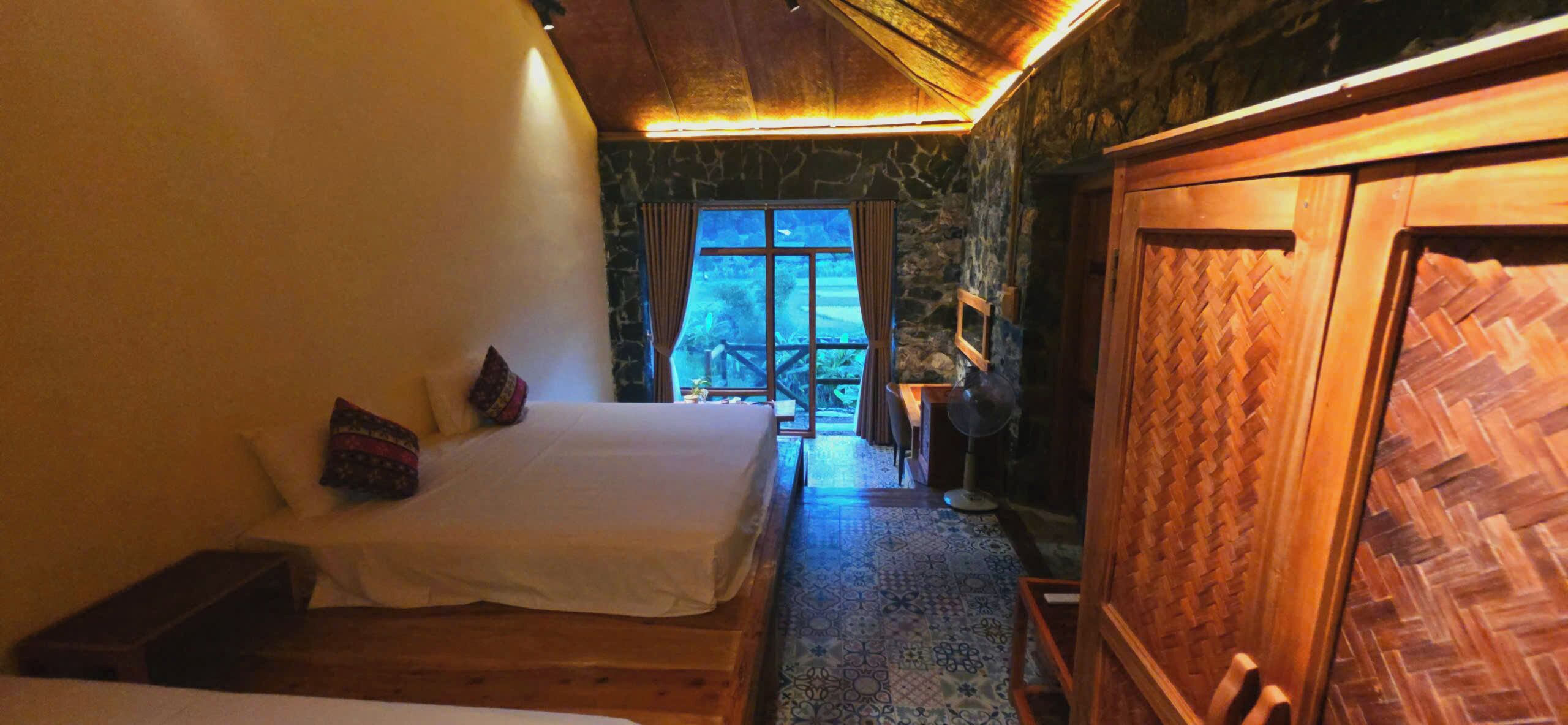 A room with two beds, a wooden wardrobe, and a stone wall.