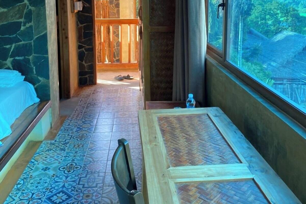 A room with a view of a tropical landscape, a wooden table, and patterned floor tiles.