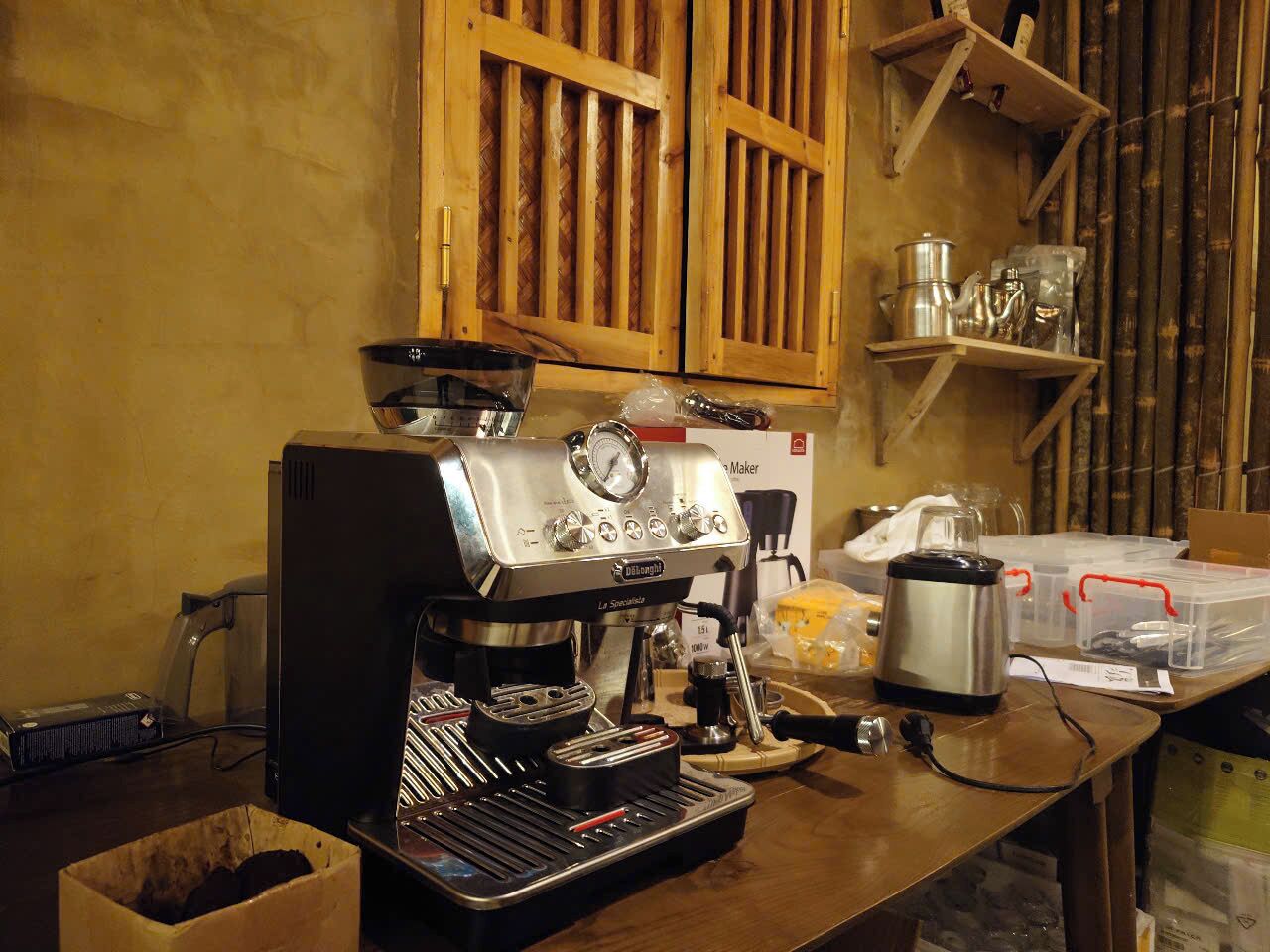 Eine Kaffeemaschine steht auf einem Holztisch in einer Küche mit Bambuswänden und Regalen.