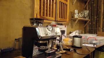 Eine Kaffeemaschine steht auf einem Holztisch in einer Küche mit Bambuswänden und Regalen.